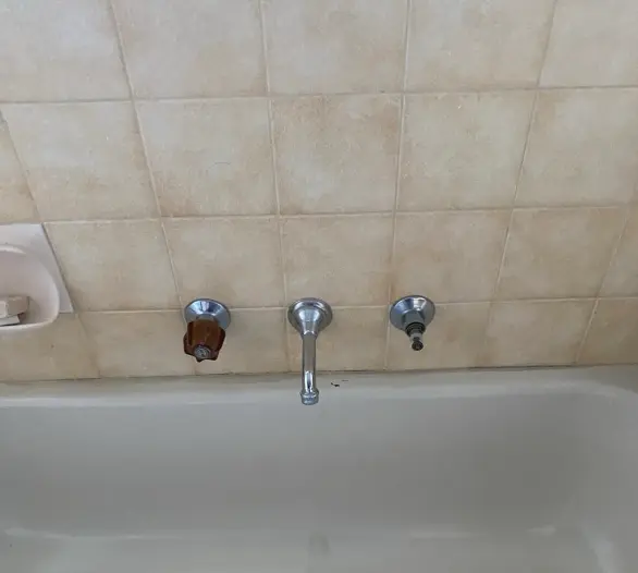 Wall-mounted bath taps and spout over a cream bath with beige tiles