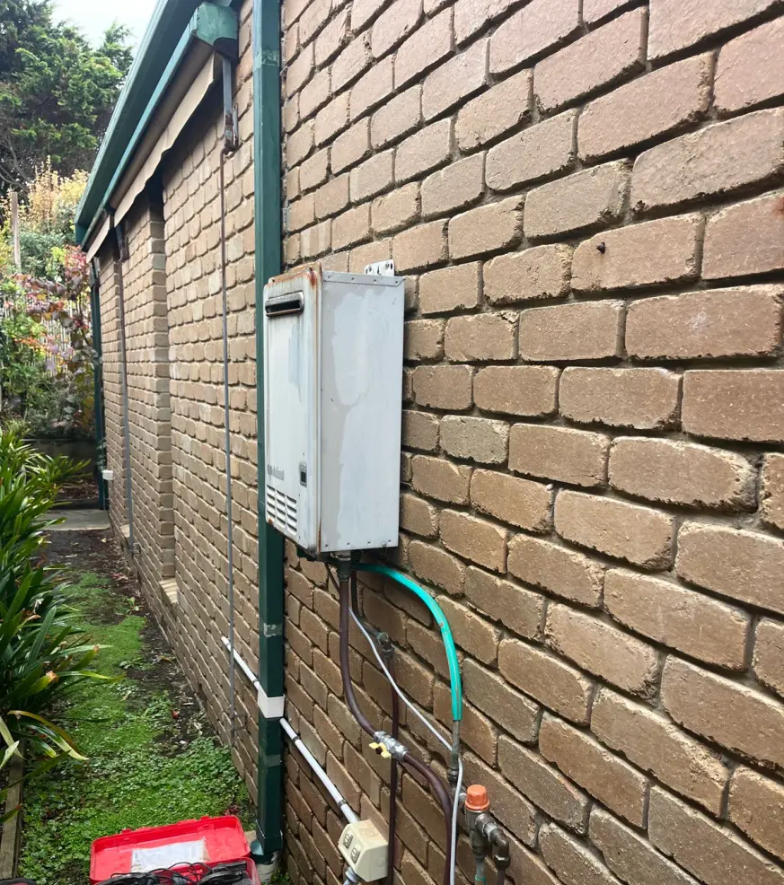 Wall-mounted hot water unit on a brick wall with pipework and open red toolboxes below