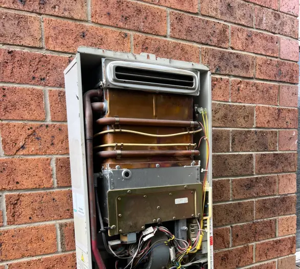 Wall-mounted hot water unit with its cover removed, showing internal pipes and the burner assembly