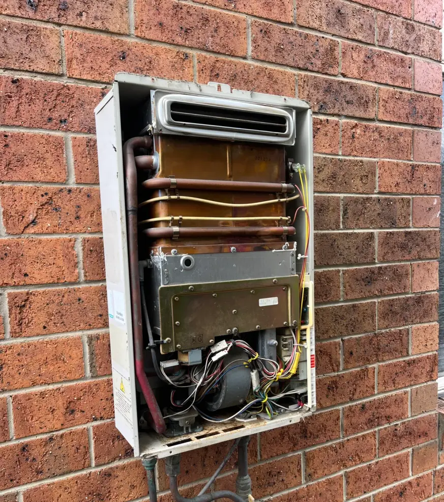 Wall-mounted hot water unit with its cover removed, showing internal pipes and the burner assembly