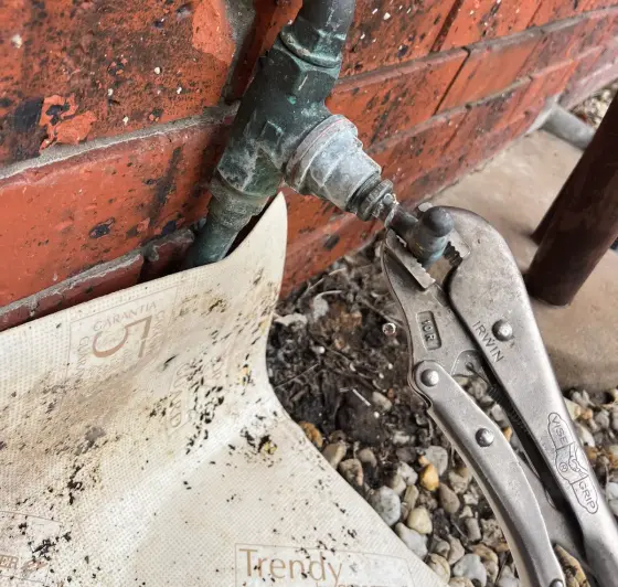 Weathered brass outdoor tap on a brick wall with locking pliers beside it