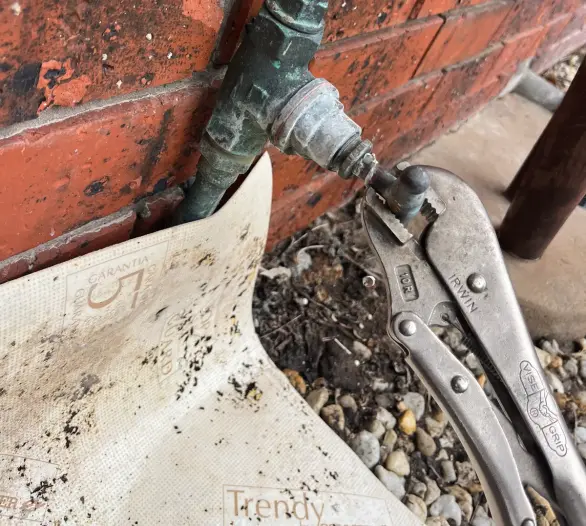 Weathered brass outdoor tap on a brick wall with locking pliers beside it