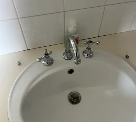 White basin with chrome hot and cold handles and a spout against a white tiled wall