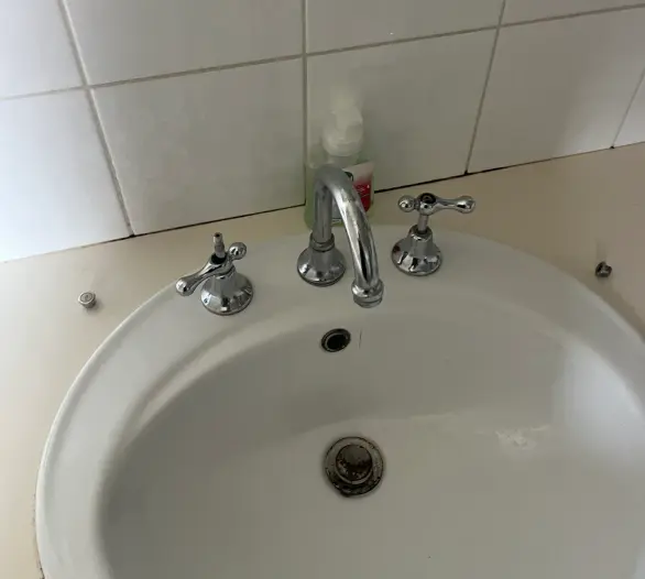 White basin with chrome hot and cold handles and a spout against a white tiled wall