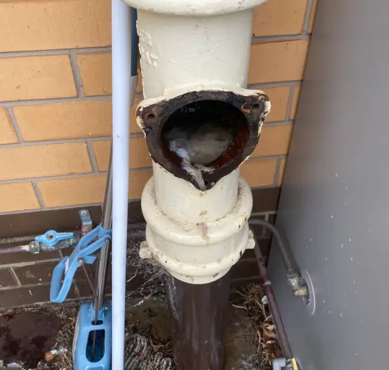 White cast iron pipe with an open rusty inspection port, jetter gear and a hot water unit beside it