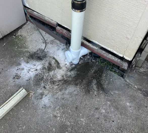 White pipe with a rubber coupling and junction at the foot of a weatherboard wall, stained concrete below