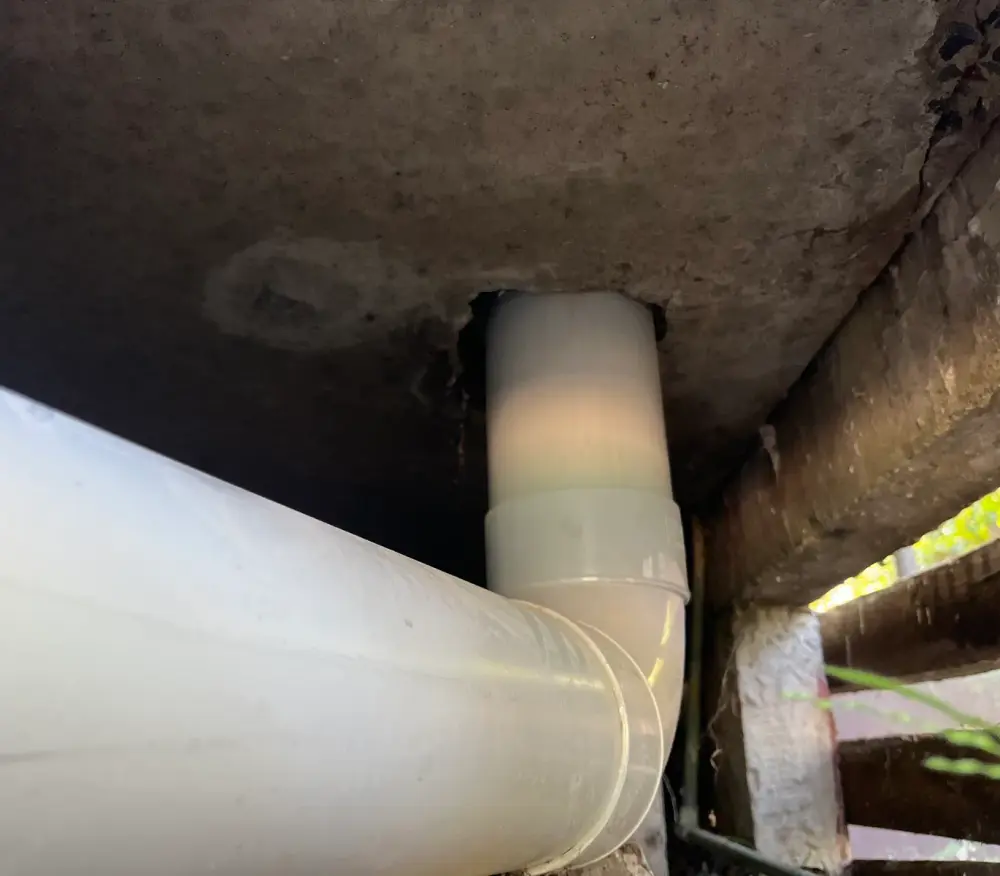 White PVC elbow and large pipe in a dark gap under a concrete slab
