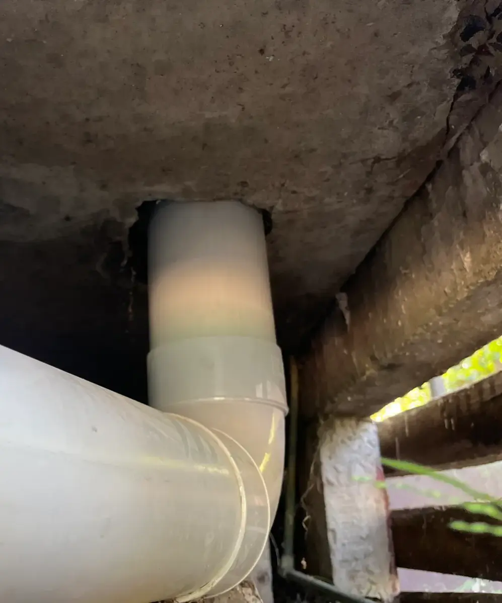 White PVC elbow and large pipe in a dark gap under a concrete slab