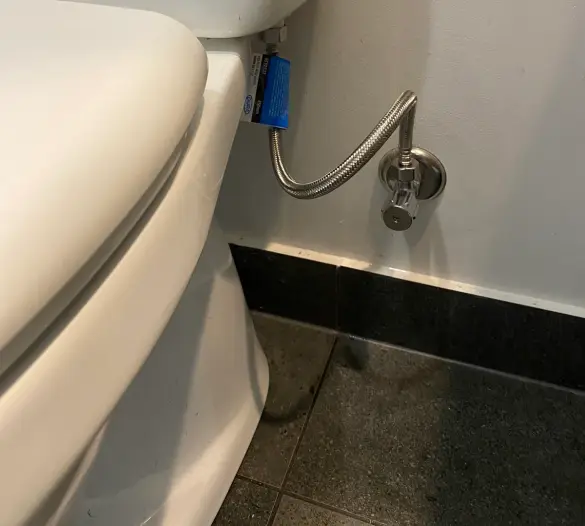 White toilet cistern with a braided flexible hose connected to a wall isolation tap