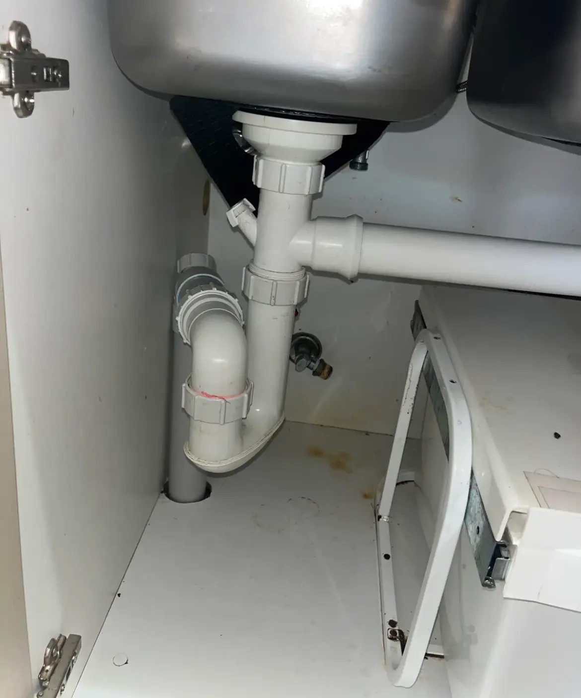 White waste pipes and trap under a sink beside a dishwasher