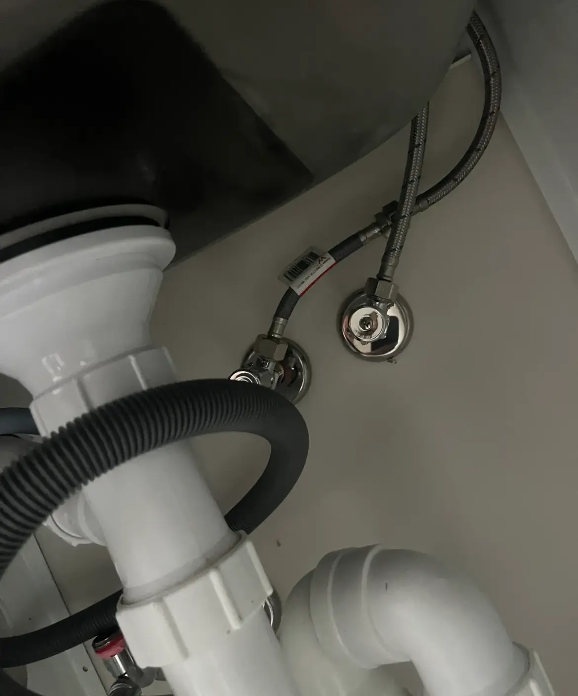 White waste pipework and braided hoses under a sink