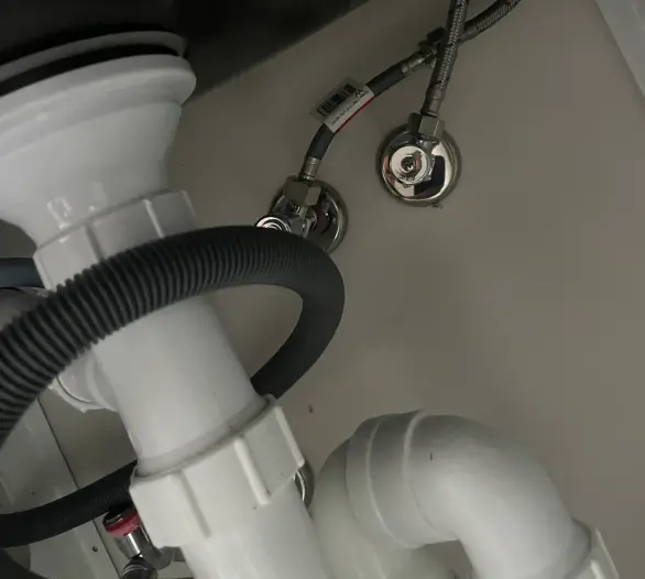 White waste pipework and braided hoses under a sink