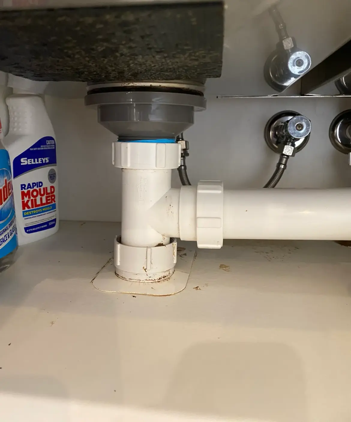 White waste pipework and trap under a sink with cleaning products beside it