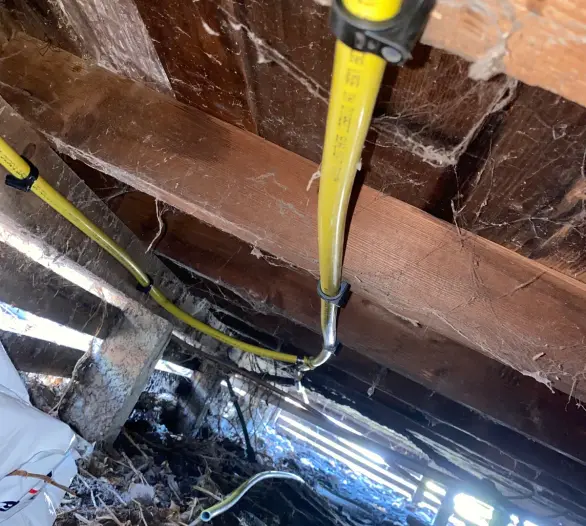 Yellow gas pipe running through a subfloor with a work boot nearby